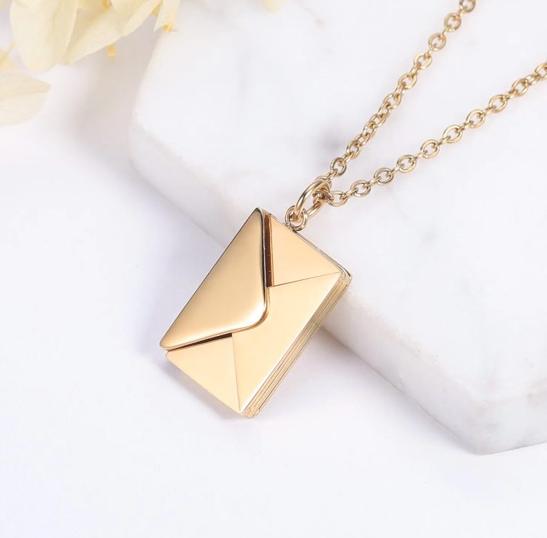 Gold envelope necklace on a chain with a marble background.